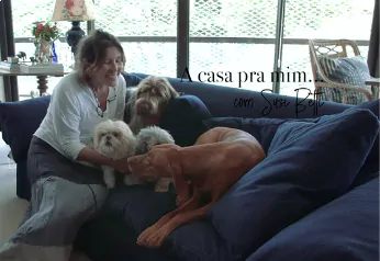 Uma mulher radiante brinca com ternura com seus três adoráveis cachorros, todos reunidos em um sofá azul.