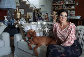 Uma mulher está sentada confortavelmente em um sofá, em uma sala decorada de forma acolhedora, com um adorável cachorro deitado ao seu lado.